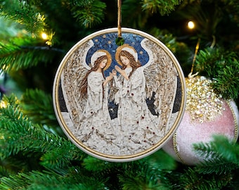 May include: Round Christmas ornament featuring a mosaic design of two angels with wings, halos, and white robes. The background is a starry night sky. The ornament is hanging on a Christmas tree with other ornaments.