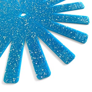 May include: A close-up of a fan of ten turquoise blue glitter sheets. The sheets are arranged in a radial pattern, with the tips of the sheets pointing outwards.