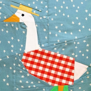 Könnte beinhalten: Ein skurriler Quiltblock mit einem Gänsemotiv. Die Gans hat einen weißen Kopf und Hals, einen orangefarbenen Schnabel und einen rot-weiß karierten Körper. Sie trägt einen Strohhut vor einem blauen Hintergrund mit weißen Sternen.