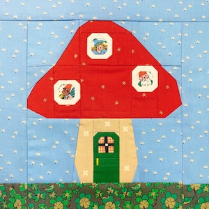 May include: A red and white mushroom-shaped house with a green door and three windows. The windows have images of people inside. The house is sitting on a green and brown patterned fabric.