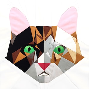 Puede incluir: Un diseño de colcha de retazos de la cara de un gato con orejas rosas, ojos verdes y piezas de tela marrón, negro, blanco y gris.