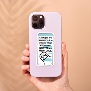 Anti-AI Duck Sticker - Anti AI Sticker, Ducking Autocorrect, No AI Art, Funny Duck, Fuck ai, Funny Swear Words, Funny Inappropriate Stickers. Inspired when I was joking with my husband, this sticker says "I thought we learned not to trust AI when autocorrect INSISTED we meant DUCK" over a background of a phone text conversation. A skeptical duck hangs out at the bottom of the screen.