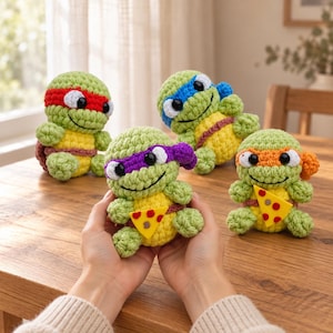May include: Four small, handmade crochet turtle dolls featuring light green bodies and yellow bellies. Each turtle wears a different colored mask: red, blue, purple, or orange. One turtle holds a small, yellow felt pizza slice with red pepperoni.