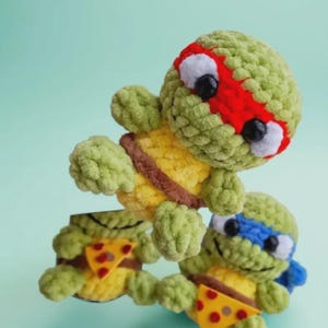 May include: Crocheted Teenage Mutant Ninja Turtles in green, yellow, and brown. Each turtle has a different colored mask: red, blue, and brown. They are holding pizza slices. The turtles are handmade.