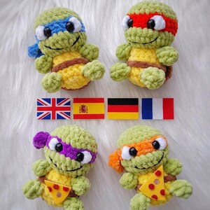 May include: Four crocheted turtle plushies made of light green yarn with yellow bellies and brown shells. Each wears a different colored eye mask: blue, red, purple, and orange. Two turtles hold small felt pizza slices. Four national flags are centered.