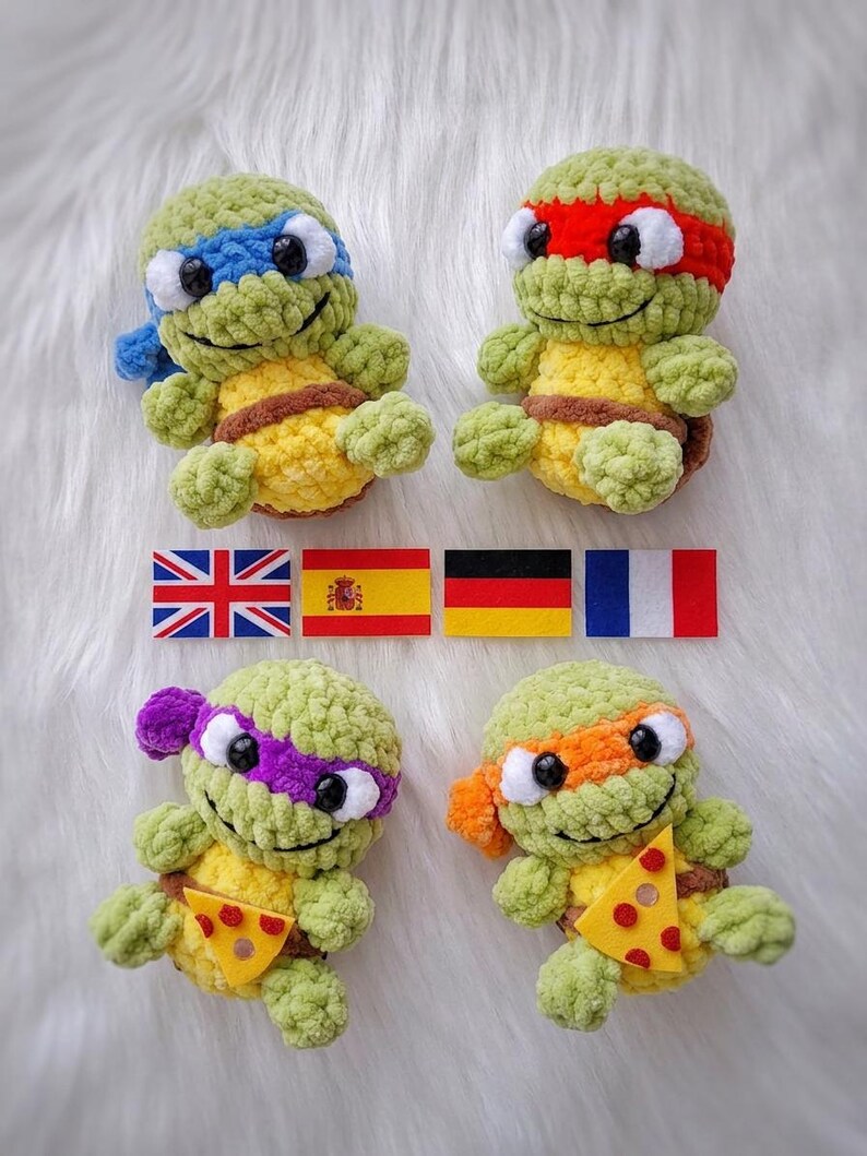 May include: Four crocheted turtle plushies made of light green yarn with yellow bellies and brown shells. Each wears a different colored eye mask: blue, red, purple, and orange. Two turtles hold small felt pizza slices. Four national flags are centered.