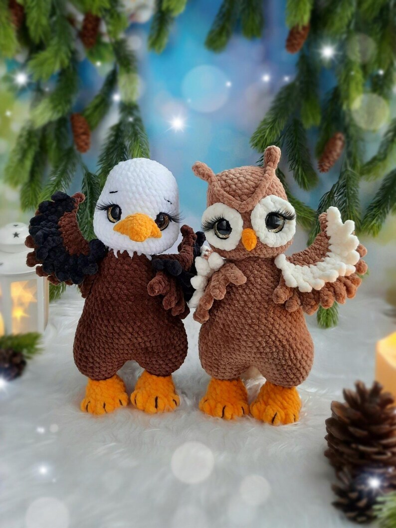 May include: Two crocheted plush toys featuring a bald eagle and an owl. The eagle has a white head, brown body, black wings, and orange feet. The owl is brown with white eye patches, a small orange beak, and orange feet. Both have large eyes.