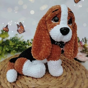 Peut inclure: Un chien en peluche fait &agrave; la main, avec des accents marron, blancs et noirs. Le chien a de grandes oreilles tombantes, un museau blanc et un nez noir. Il est assis sur un tapis tress&eacute;, avec des papillons en arri&egrave;re-plan. Le chien mesure environ 25 cm de haut.