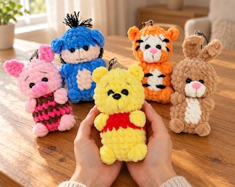 May include: A collection of five small, plush, crocheted animal keychains featuring a yellow bear in a red shirt, a pink pig, a blue donkey, an orange tiger with black stripes, and a brown rabbit, all with black plastic eyes and metal clips.