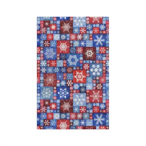 May include: A rectangular fabric piece featuring a patchwork design of various square blocks in shades of red, dark blue, and light blue. Each square contains a unique white snowflake pattern, creating a dense, repeating winter-themed motif.