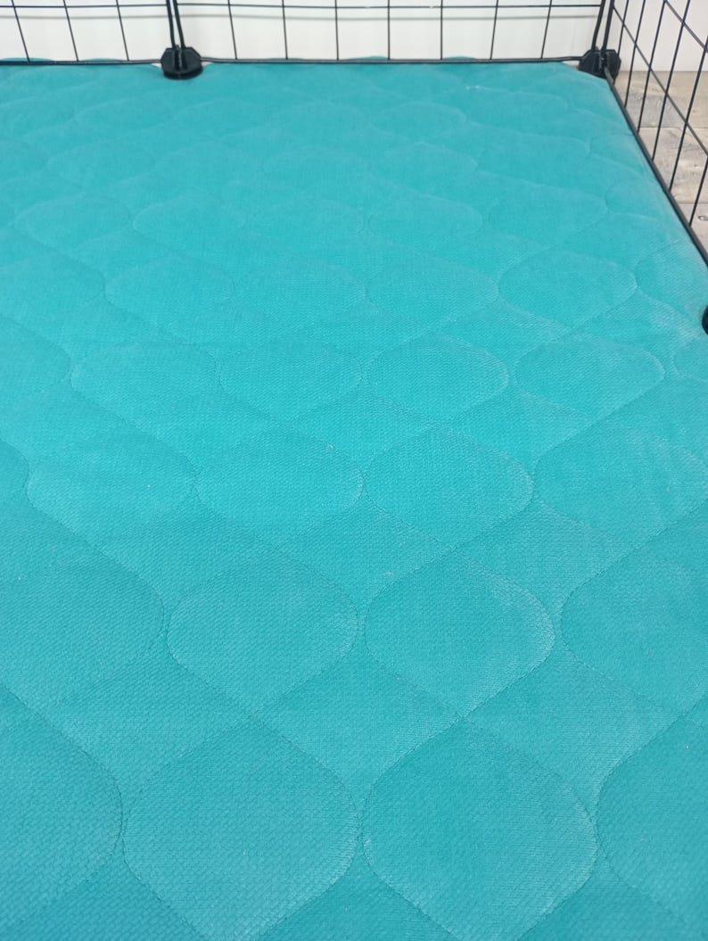 May include: A turquoise blue quilted cage liner with a diamond pattern. The liner is made of a soft, durable material and is designed to protect the bottom of the cage from scratches and dirt.