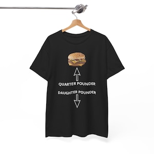 Puede incluir: Camiseta negra con un gráfico blanco de una hamburguesa y el texto "Quarter Pounder" y "Daughter Pounder" con flechas apuntando hacia arriba y hacia abajo.