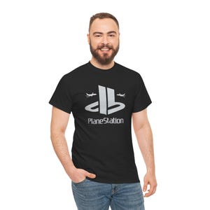 May include: Black t-shirt with a silver graphic that says "PlaneStation". The graphic is a parody of the PlayStation logo, with two airplane silhouettes replacing the stars. The shirt is made of a soft material.