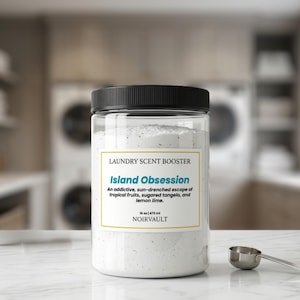 May include: A clear plastic jar with a black lid, labeled "LAUNDRY SCENT BOOSTER" and "Island Obsession." The label describes a tropical scent. The jar contains white powder and sits on a white surface with a small metal scoop.