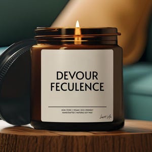 May include: A brown glass candle with a white label that reads "Devour Feculence". The label also includes the text "Non-Toxic | Vegan | Eco-Friendly | Handcrafted | Natural Soy Wax". The candle is lit and has a small flame.