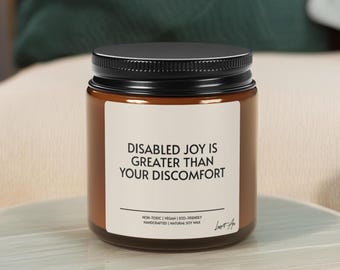 May include: A brown glass jar candle with a black lid. The label reads "DISABLED JOY IS GREATER THAN YOUR DISCOMFORT." Additional text includes "NON-TOXIC | VEGAN | ECO-FRIENDLY HANDCRAFTED | NATURAL SOY WAX."