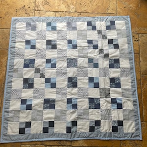 May include: A blue and white patchwork quilt with a light blue border. The quilt is made up of squares of different fabrics, some with patterns and some plain.