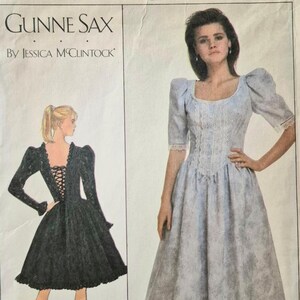 May include: A sewing pattern envelope for Gunne Sax by Jessica McClintock featuring two dress designs. One is a light blue floral print dress with puff sleeves and lace trim. The other is a black lace dress with a corset-style lace-up back.