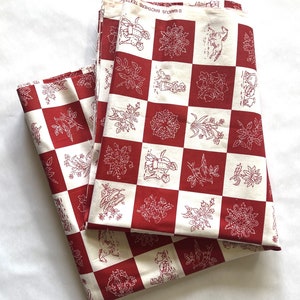May include: Two folded pieces of fabric with a red and white checkered pattern. Each square features a different white line drawing of flowers, animals, and other designs. The fabric is labeled "MARCUS BROTHERS TEXTILES".