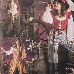 Può includere: Sono esposti tre costumi da pirata da donna. Uno indossa un cappotto rosso e pantaloni marroni, un altro un gilet rosso e pantaloni a righe, e il terzo un completo color pesca. I costumi includono cappelli, gilet e accessori.