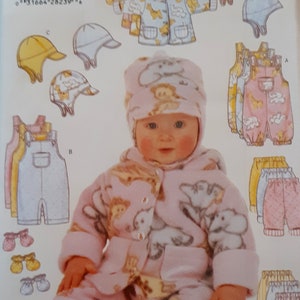 Pode incluir: Um envelope de molde de costura para roupa de bebé com ilustrações de um casaco com capuz, jardineiras, gorros e luvas. A capa mostra uma boneca a usar um casaco de lã polar rosa e um gorro a condizer com estampado de girafas e elefantes.