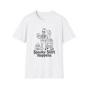 May include: A white short-sleeve t-shirt featuring a black graphic of a skeleton nurse wearing a cap, holding a clipboard, and standing next to a medical cart and a jack-o'-lantern. The text below reads Spooky Shift Happens.