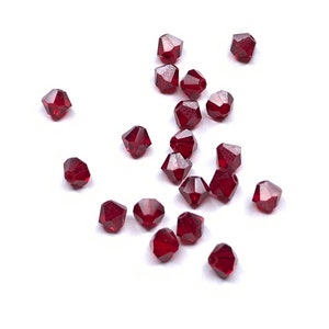 May include: A scattering of faceted, dark red beads against a white background. The beads have a geometric shape with multiple sides, reflecting light. These beads are suitable for jewelry making and crafting projects.