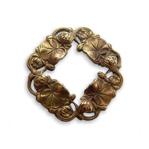 May include: A decorative brass-colored metal ring with a floral design. The ring is composed of four sections, each featuring leaves and flower buds. The design is symmetrical and detailed, with a vintage aesthetic.