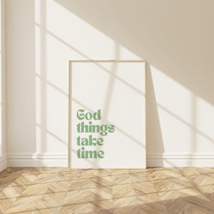 Puede incluir: Una impresión enmarcada con el texto "God things take time" en una fuente verde sobre un fondo blanco. La impresión está colgada en una pared blanca con un suelo de madera.