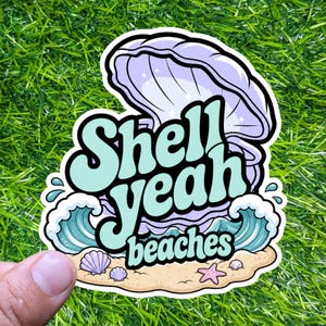 May include: A die-cut sticker featuring a light purple open seashell with a pearl inside, set against a sandy beach with turquoise ocean waves. The text "Shell yeah beaches" is written in a bold, light blue font across the center of the design.