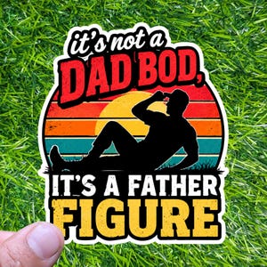 Op de afbeelding: Een sticker met de tekst "It's not a DAD BOD, It's a FATHER FIGURE." Het ontwerp toont een silhouet van een man die ligt, tegen een zonsondergang achtergrond van oranje, rode en teal strepen.