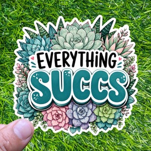May include: A die-cut sticker featuring a variety of colourful succulents in shades of green, pink, and purple. The text "EVERYTHING SUCCS" is printed in bold, dark letters in the centre, surrounded by a detailed illustration of various plants.
