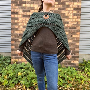 Puede incluir: Un poncho de crochet verde con un patr&oacute;n de diamante. El poncho se lleva sobre un su&eacute;ter marr&oacute;n y unos vaqueros azules.