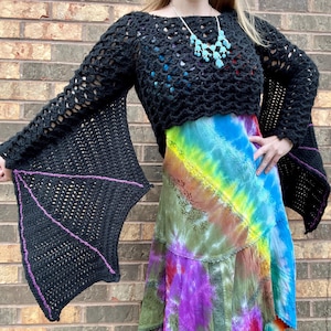 May include: Black crochet top with bat wing sleeves. The sleeves are lined with purple yarn. The top is cropped and has a loose fit.