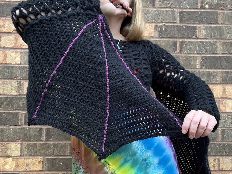 May include: Black crochet top with a bat wing design. The top has a large open stitch pattern and is accented with purple yarn.