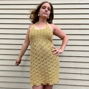 May include: A yellow crochet halter dress with a delicate pattern. The dress is sleeveless and has a fitted bodice and a flowing skirt.