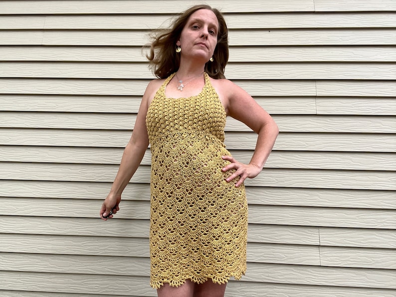 May include: A yellow crochet halter dress with a delicate pattern. The dress is sleeveless and has a fitted bodice and a flowing skirt.