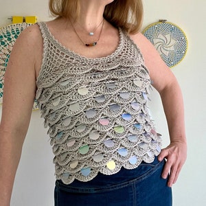 May include: A crocheted tank top with a scalloped hem and iridescent sequins. The top is a light beige color and the sequins are in shades of blue, green, pink, and yellow.