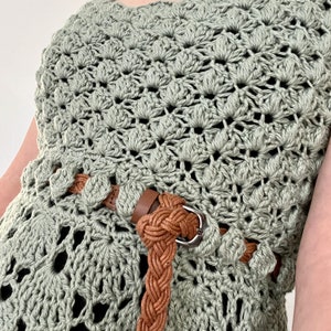 May include: A sage green crochet top with a brown braided belt. The top has a delicate openwork pattern.