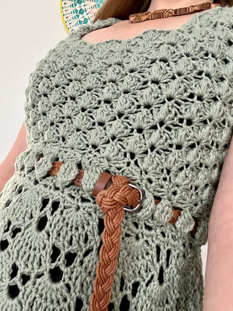 May include: A sage green crochet top with a brown braided belt. The top has a delicate openwork pattern.