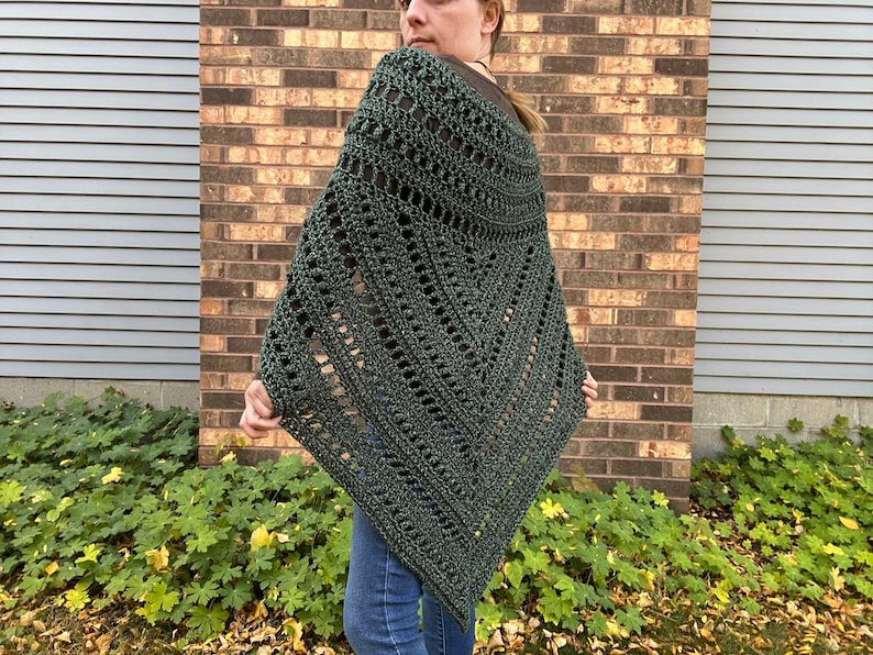 Puede incluir: Un poncho de crochet verde oscuro con un patr&oacute;n de encaje. El poncho lo lleva puesto una persona de pie frente a una pared de ladrillo.