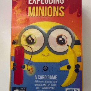 May include: A rectangular game box for Exploding Minions, featuring a yellow character with large goggles, holding a red stick of dynamite and a yellow banana. The box displays the title, game details, and the Exploding Kittens logo.