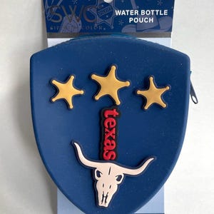 May include: A blue shield-shaped water bottle pouch featuring three yellow stars, the word "texas" in red letters, and a white longhorn skull graphic. The packaging text reads "SWC SIP WITH COLOR," "WATER BOTTLE POUCH," and "FITS WATER BOTTLES AND TUMBLERS 20 OZ, 30 OZ, 40 OZ."