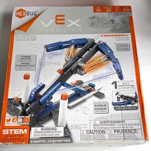 以下が含まれることがあります： 青、グレー、オレンジのプラスチック製クロスボウモデルが描かれたHexbug Vex Robotics Crossbow組み立てキットの箱。パッケージには技術図面、Crossbow Launcherの文字、13メートル以上飛ばせるという記載があります。
