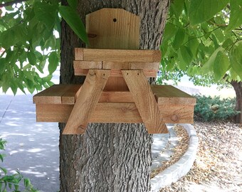 May include: A wooden bird feeder shaped like a miniature picnic table attached to a tree trunk.