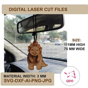 Puede incluir: Un adorno de madera de color marrón claro con forma de dinosaurio triceratops colgado del espejo retrovisor de un coche. El texto dice DIGITAL LASER CUT FILES, SIZE: 111MM HIGH 75 MM WIDE, MATERIAL WIDTH: 3 MM, SVG-DXF-AI-PNG-JPG. El dinosaurio sonríe.