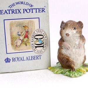 May include: A ceramic mouse figurine with brown fur and a white chest, standing on a green leaf base. Beside it is a light blue box labeled THE WORLD OF BEATRIX POTTER and ROYAL ALBERT, featuring an illustration of a duck and a fox, plus a 100-year seal.