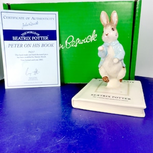 Peut inclure: Une figurine en céramique de Pierre Lapin portant une veste bleu clair, debout sur une base rectangulaire blanche en forme de livre avec le texte Beatrix Potter. Inclut un certificat d'authenticité et une boîte verte marquée John Beswick.
