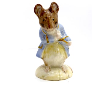 May include: A ceramic mouse figurine, wearing a light blue jacket with gold detailing. The mouse has brown fur and stands on a small, round base. A collectible item, the figurine is likely a character from a children's story.