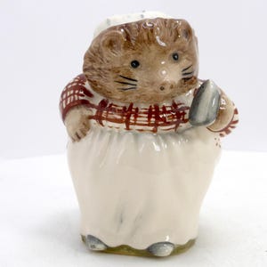 May include: A ceramic figurine of a hedgehog chef wearing a white chef's hat and a red and brown plaid shirt. The hedgehog is holding a gray spatula and wearing a white apron. The figurine has a whimsical, cartoonish design.